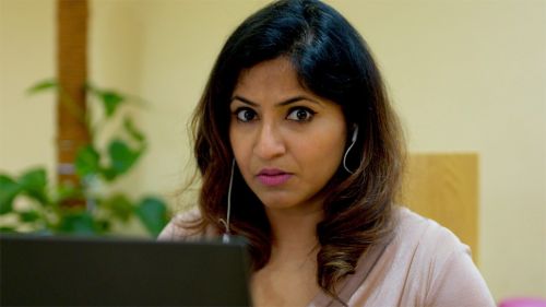 A woman sitting at a laptop, she looks directly at the camera with a confused expression on her face.