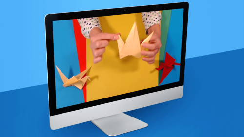Computer monitor displaying hands folding an origami paper crane against a colourful background.