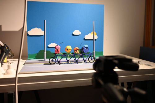 Behind the scenes photo of a selection of paper shape characters set up on a tandem bike. 